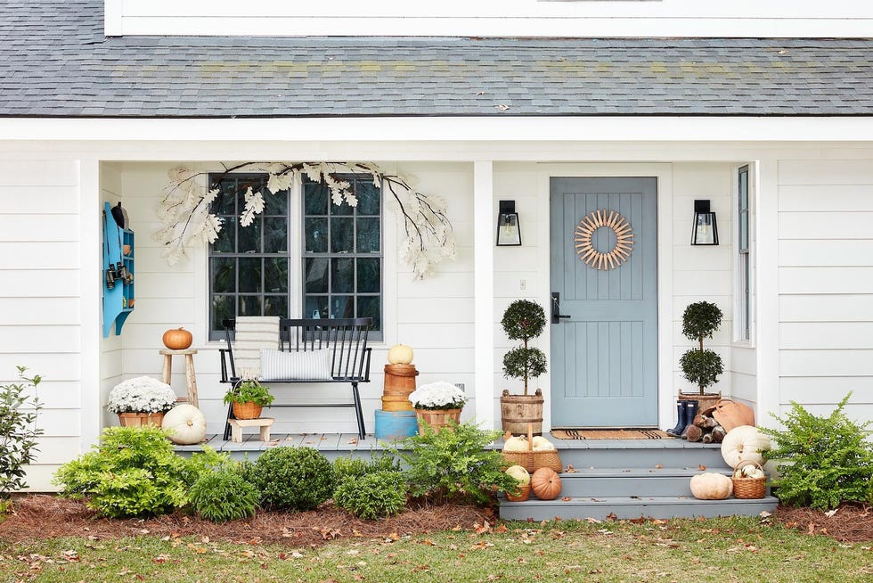 white farmhouse front porch decorated for fall with paper leaf garland, white mums and heirloom pumpkins, shaker peg wreath