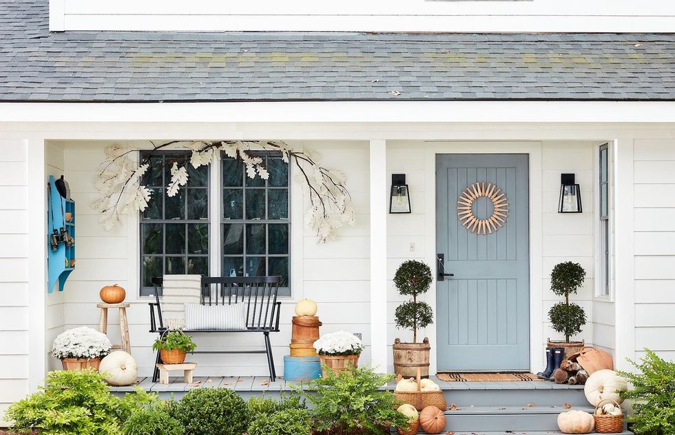 white farmhouse front porch decorated for fall with paper leaf garland, white mums and heirloom pumpkins, shaker peg wreath