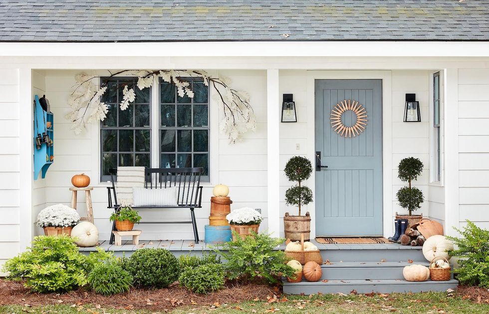 white farmhouse front porch decorated for fall with paper leaf garland, white mums and heirloom pumpkins, shaker peg wreath