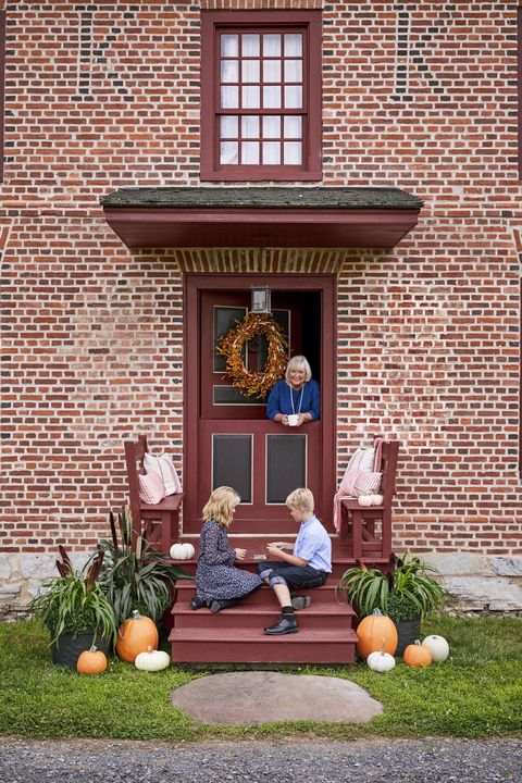 brick home with small front porch with built in benches decorated with pillows and pumpkins for fall