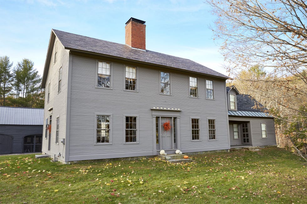 gray farmhouse with a orange floral fall front door wreath and pumpkins on front porch steps