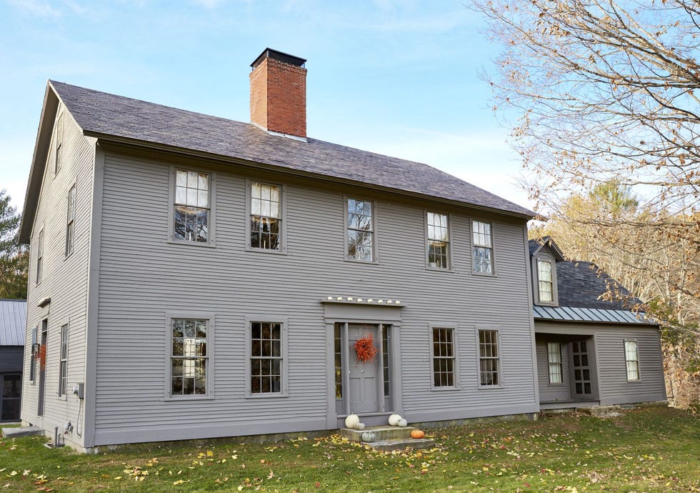 gray farmhouse with a orange floral fall front door wreath and pumpkins on front porch steps