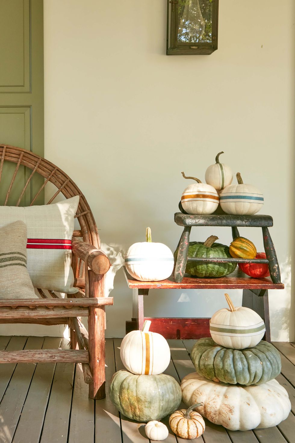 fall front porch decor featuring pumpkin stacks adorned with ribbon stripes beside bench with grain sack covered pillows