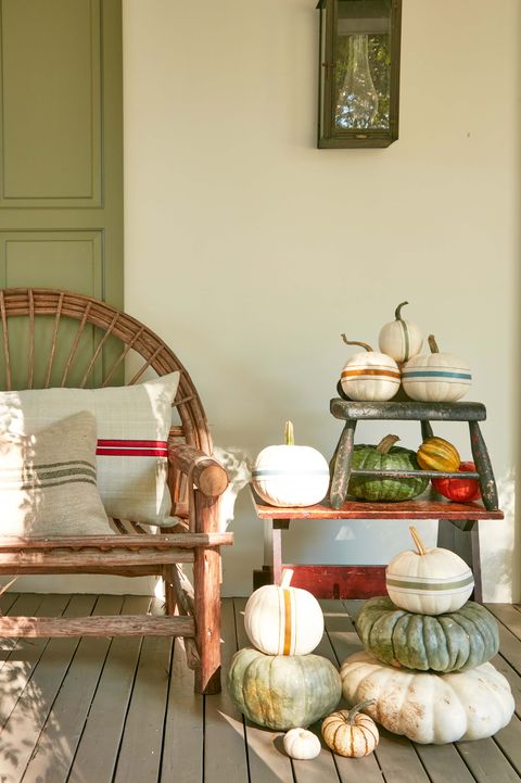 fall front porch decor featuring pumpkin stacks adorned with ribbon stripes beside bench with grain sack covered pillows