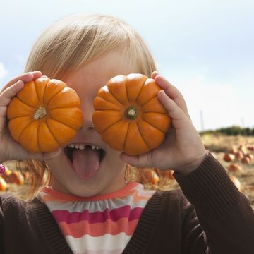 young girl covering eyes with small pumpkins and making a funny face