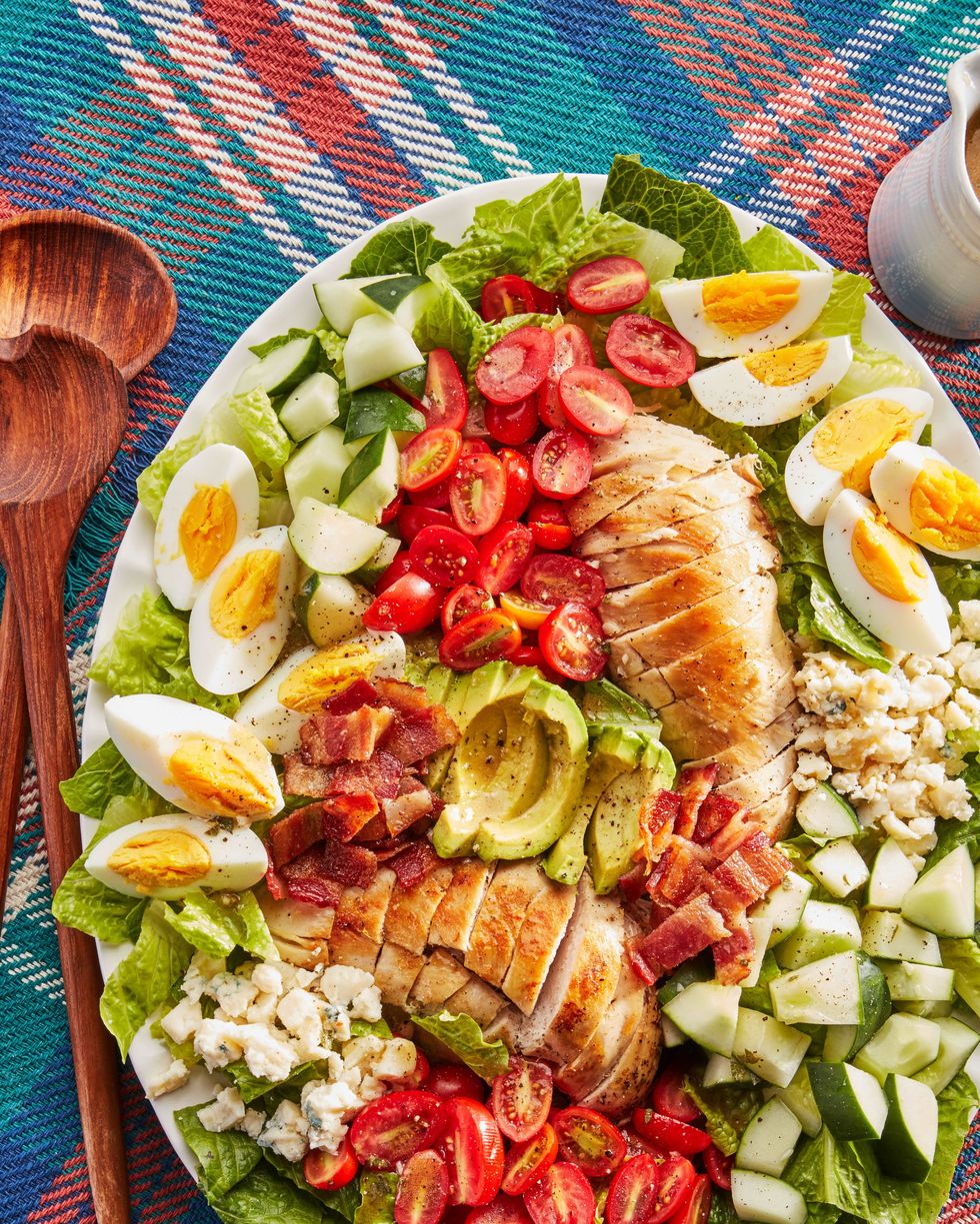 a big platter of cobb salad with chicken, tomatoes, cucumbers, hard boiled eggs, blue cheese and bacon on a bed of lettuce