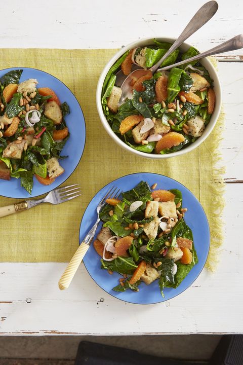 two light blue plates and one white bowl of greens and citrus salad with forks