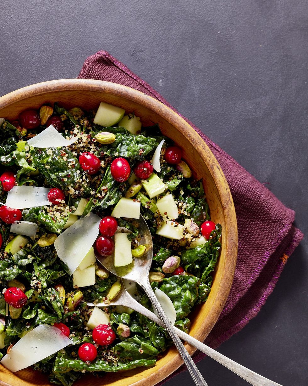 kale salad with pickled cranberries and crispy quinoa in a wooden bowl with serving utensils