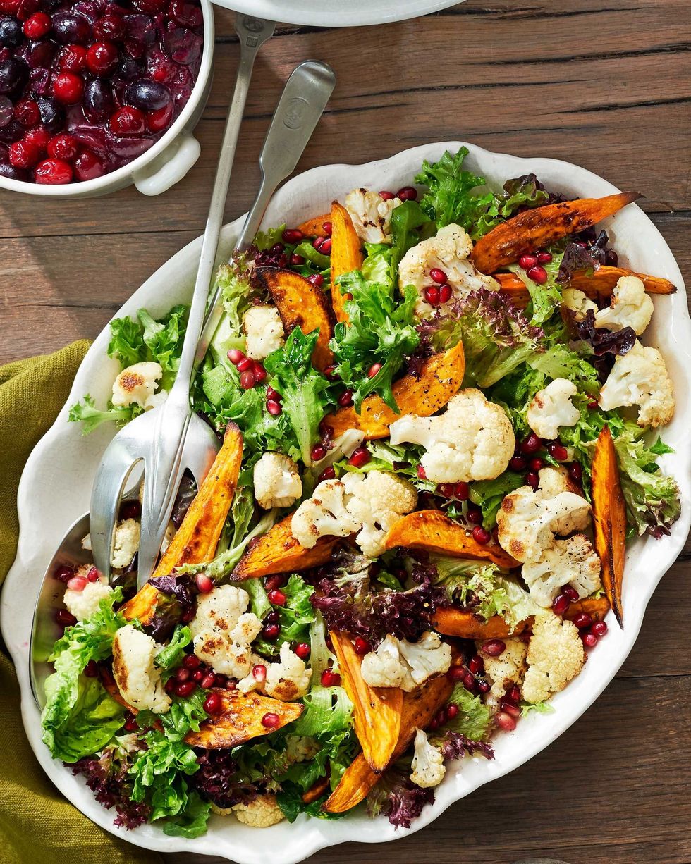 sweet potato and cauliflower salad in an oval white serving bowl with serving utensils