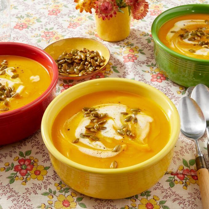 pumpkin soup in yellow bowl with pumpkin seeds and cream