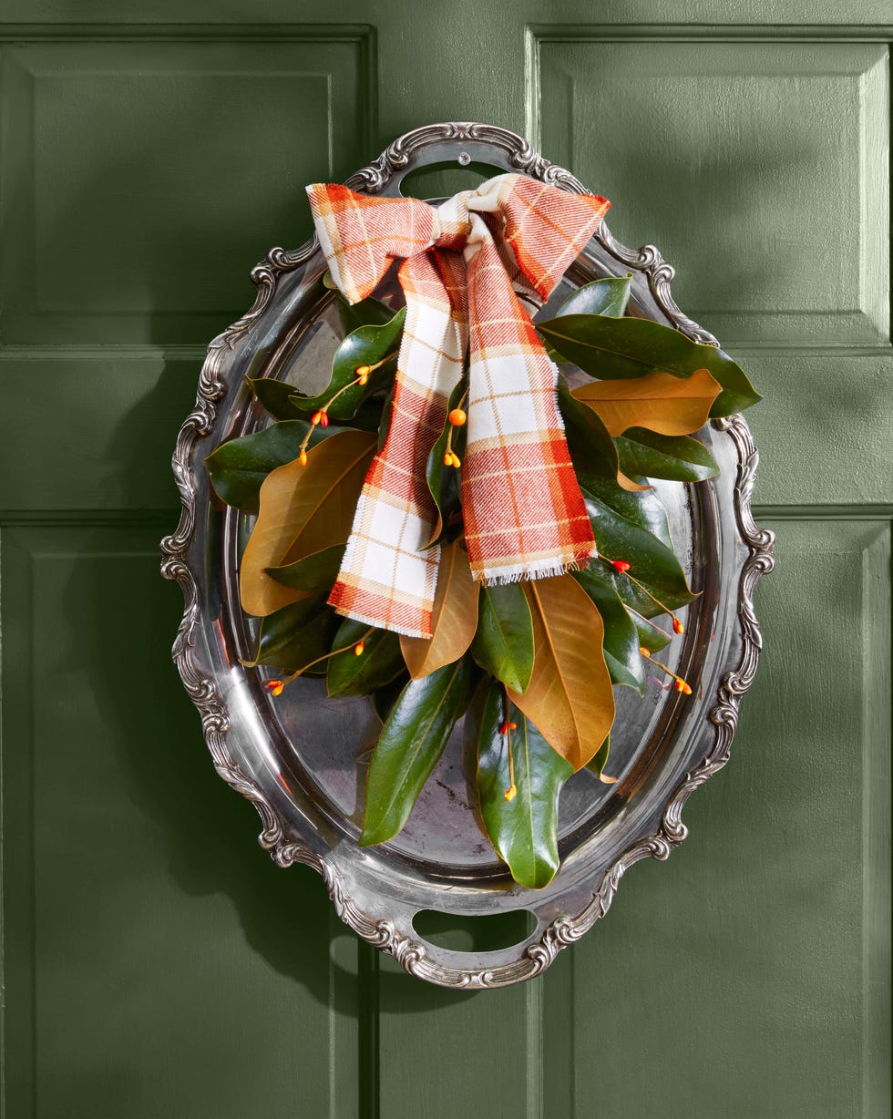 a wreath made from a silver tray with handles topped with magnolia leaves and bittersweet berries with a plaid bow