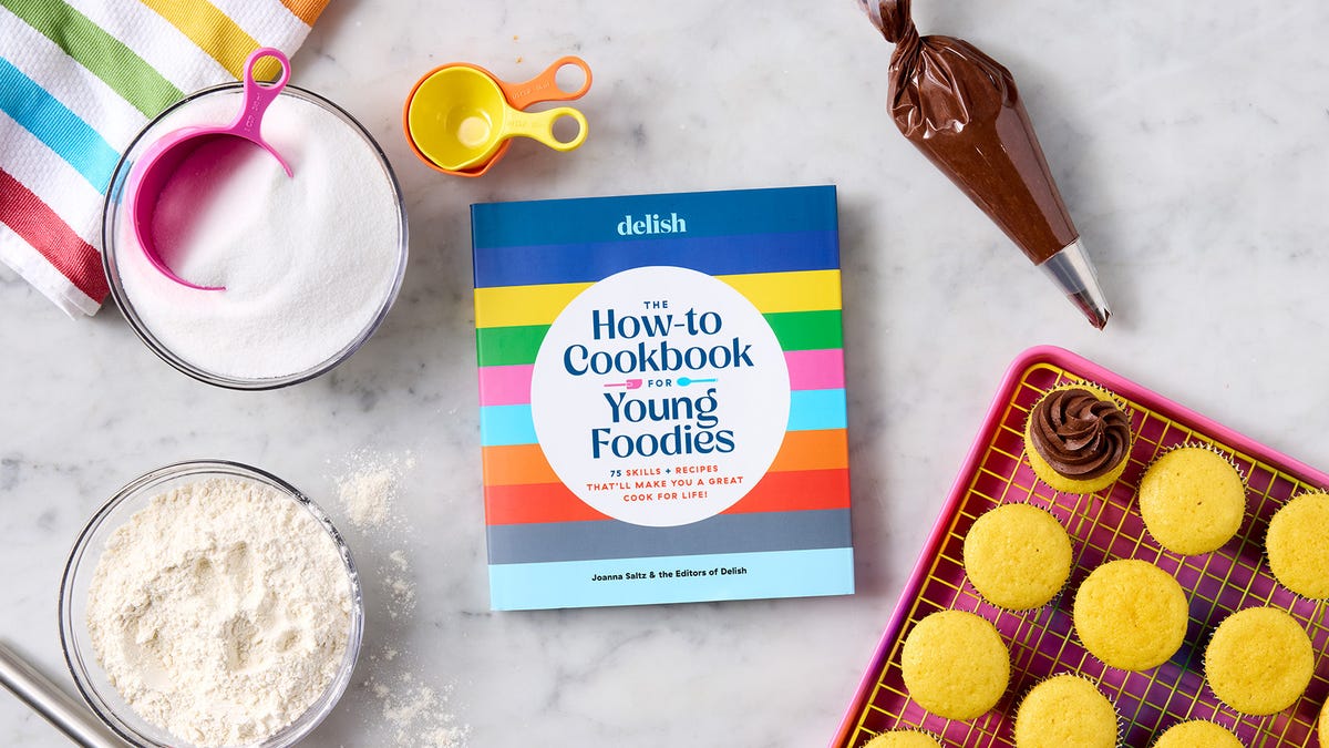 how to cookbook for young foodies against a marble surface with a tray of cupcakes, colorful measuring cups and a bowl of flour and sugar