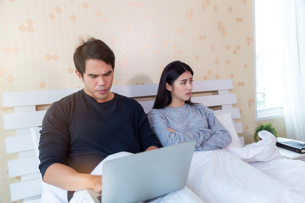 falling out of love couple in bed with man on laptop and woman staring into distance