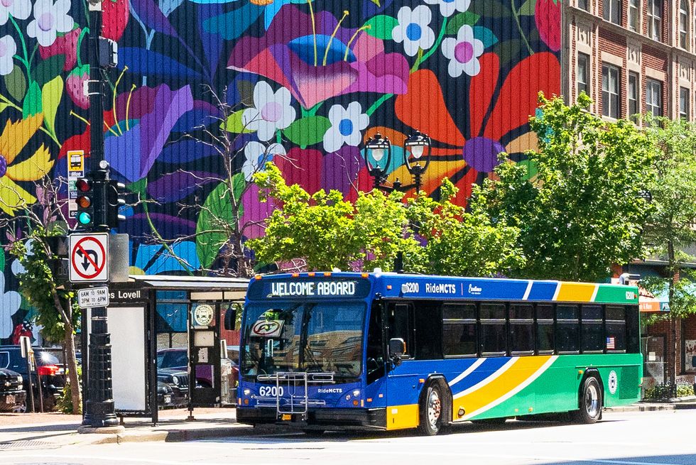 a milwaukee county transit system bus stops in front of a stop with a beautiful mural