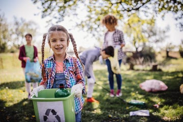 en primer plano, una niña con un cubo de basura limpiando el bosque