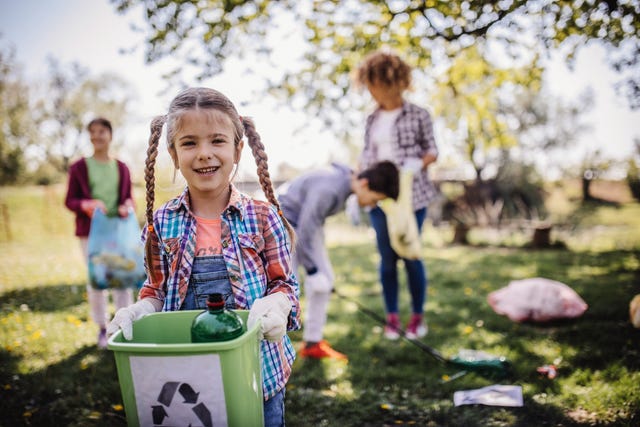 en primer plano, una niña con un cubo de basura limpiando el bosque
