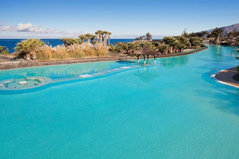 a pool with a beach and palm trees at gran meliá palacio de isora