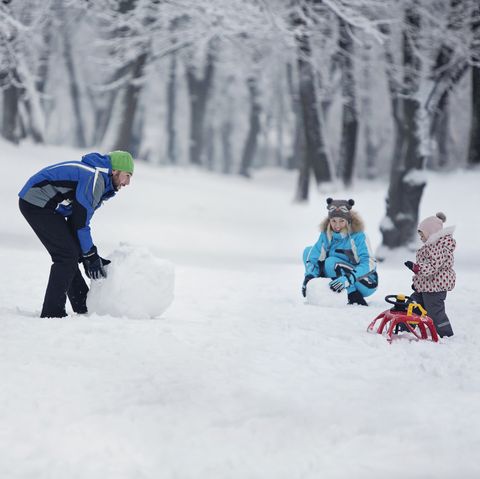 family making snowman outdoors rolling base