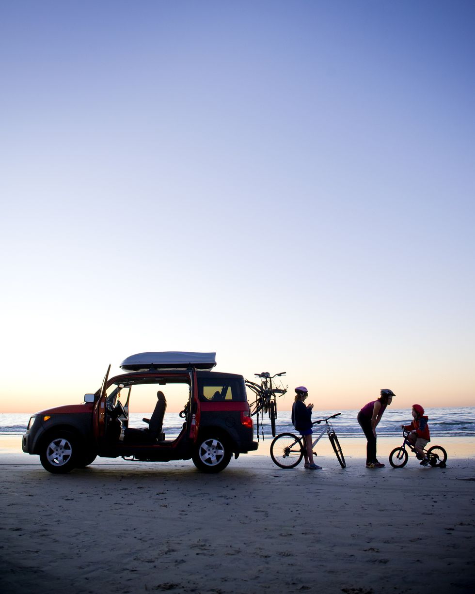silhouette of mom, dad and child on beach with car and bikes, sunset