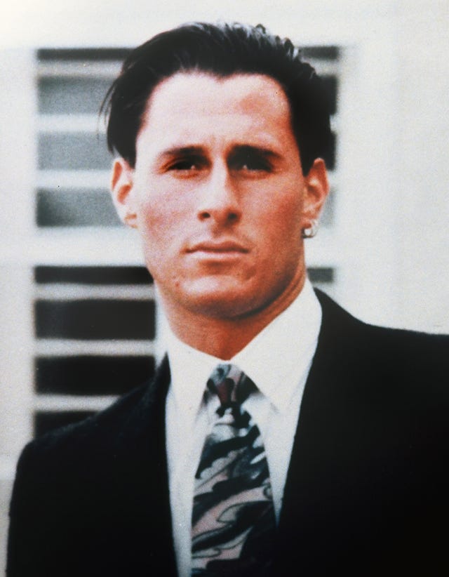 ron goldman looks at the camera, he wears a dark suit jacket, white collared shirt, patterned tie and two hoop earrings in his left ear