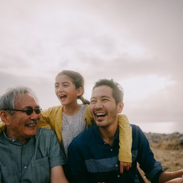 young girl having fun with her grandfather and father by sea at sunset