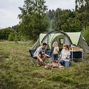 caucasian family with one child enjoying outdoor cooking over open fire on weekend camping trip in late spring