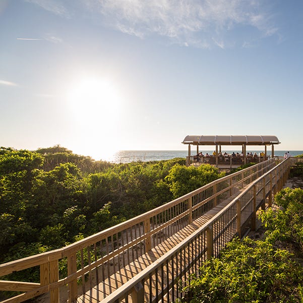 The boardwalk to the beach bar at the Ocean's Edge Resort & Golf Club, a Good Housekeeping pick for best family vacation destinations the boardwalk to the beach bar at the ocean's edge resort golf club, a good housekeeping pick for best family vacation destinations