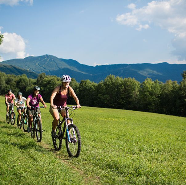 a family goes biking through green hills at smuggler's notch, a good housekeeping pick for best family vacation destinations
