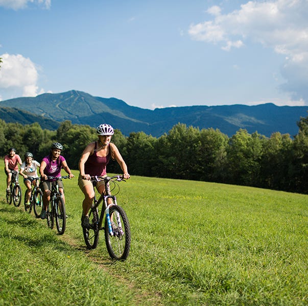 a family goes biking through green hills at smuggler's notch, a good housekeeping pick for best family vacation destinations