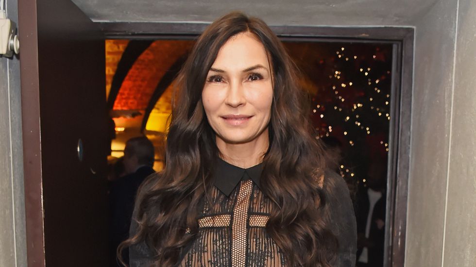 famke janssen smiles as she stands in front of an open doorway at a press event