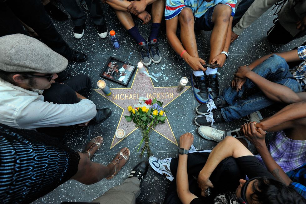 several people sit on the ground around michael jackson's star on the hollywood walk of fame, with flowers and candles on the star