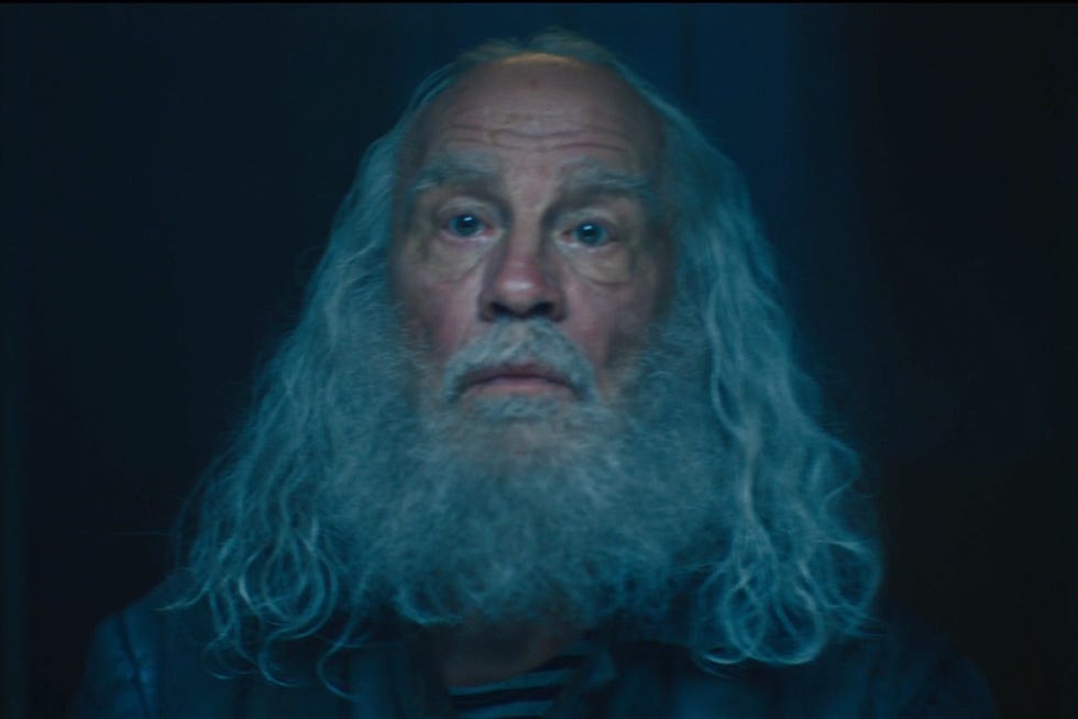 a person with long curly hair and a beard in a dark setting