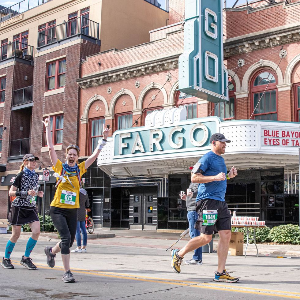 runners in the fargo marathon pass in front of a movie theater