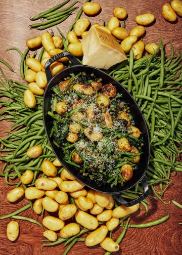 a dish with baby potatoes and green beans on a table scattered with more baby potatoes and green beans.