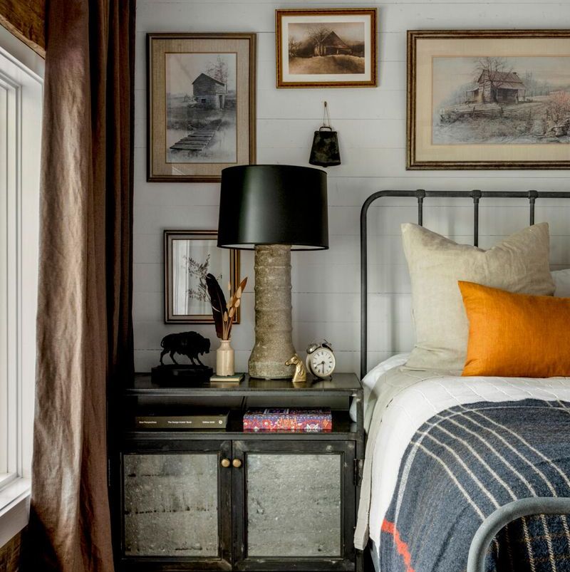 a cowbell found on the property and a collection of prints and paintings of old barns and houses adorn the wall in one of the cabin bedrooms and the walls semi transparent white stain shows off a bit of the wood grain of the tongue and groove pine
