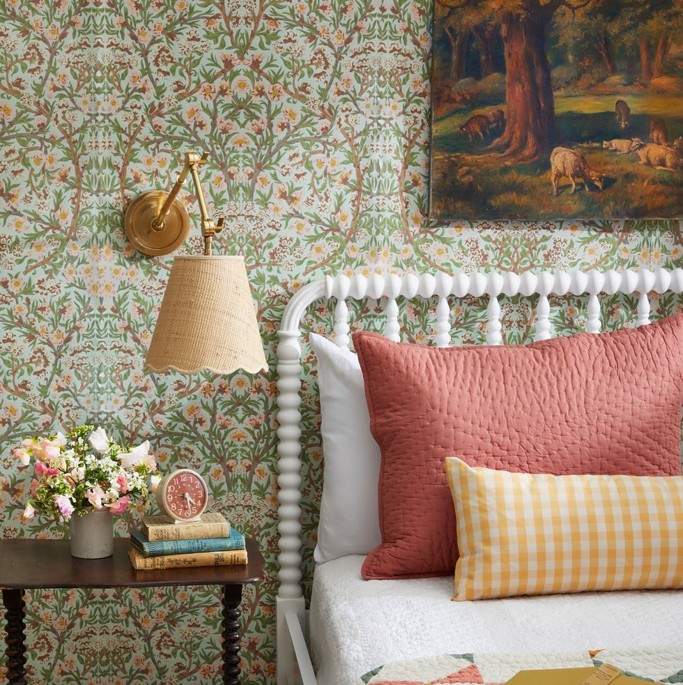a guest bedroom with floral wallpaper and a white jenny lind bed with coral and yellow pillows and quilt