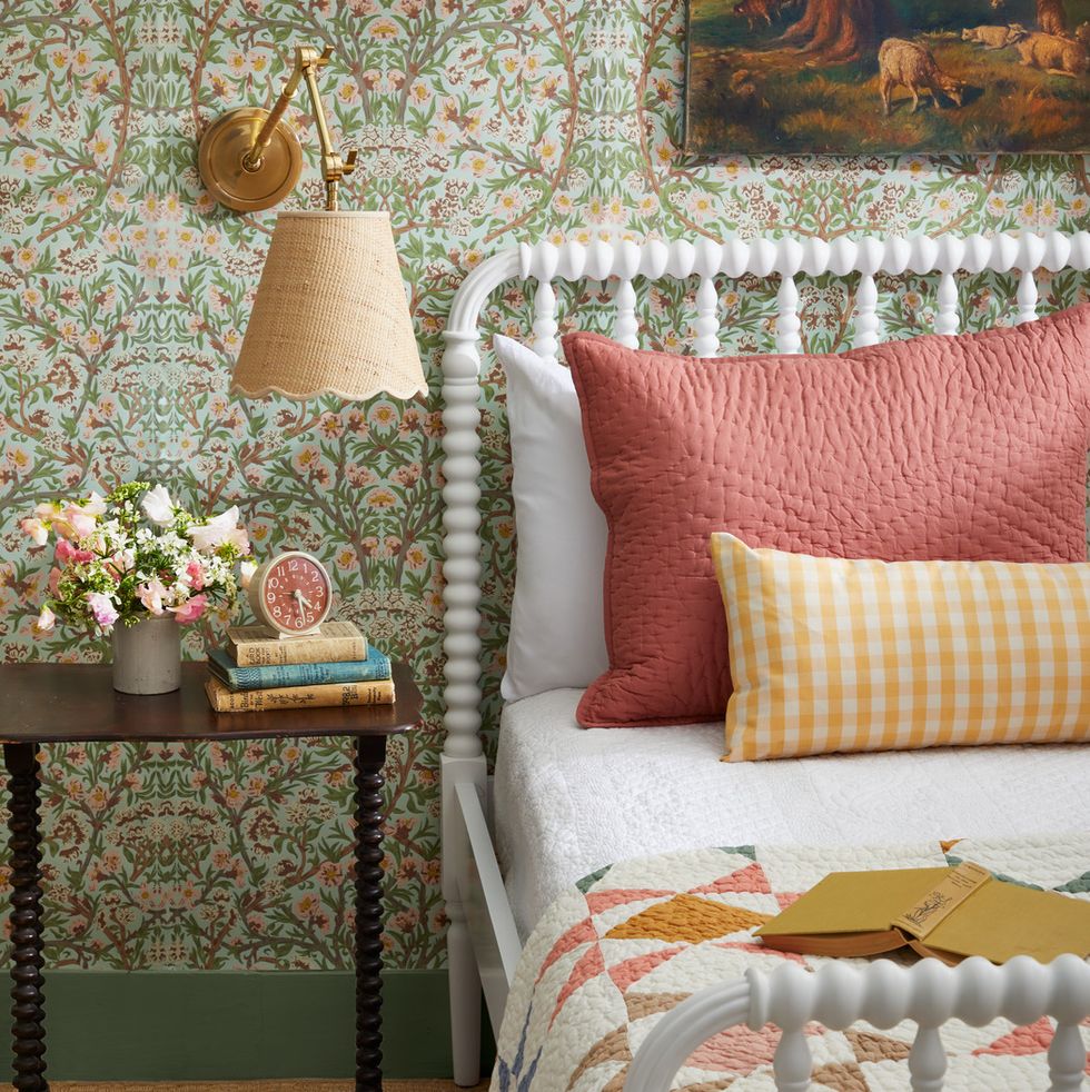 a guest bedroom with floral wallpaper and a white jenny lind bed with coral and yellow pillows and quilt