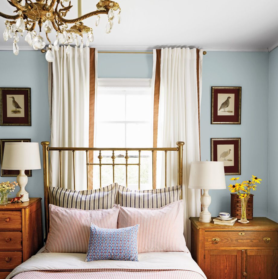 the homes red and blue palette takes a moodier turn in this bedroom with an antique brass bed with a dramatic 54 inch tall headboard that adds to the sophisticated look and mismatched dressers and 99 cent bird prints flank each side of the piece