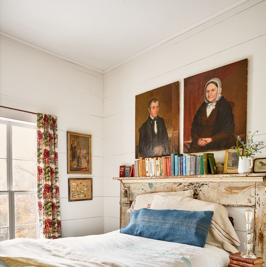 a small bedroom is packed with soulful touches like floral barkcloth curtains and a pair of antique portraits over the ned and a chippy mantel that acts as a second headboard