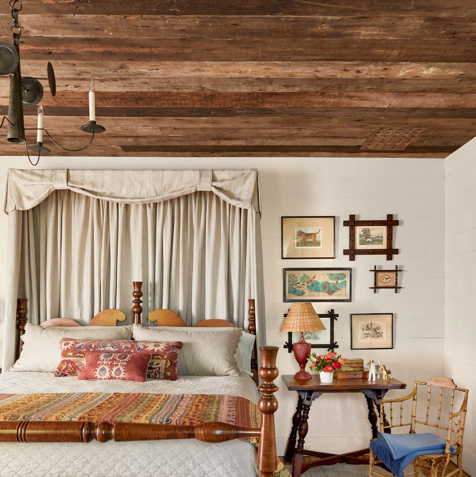a fancy farmhouse bedroom has a handmade wooden bed with a red rug on the right side and a collection of dog artwork above the bedside table