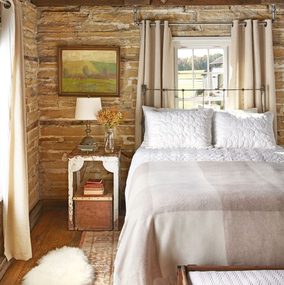 the wood slat walls and exposed ceiling in this master bedroom get an extra dose of humbleness with a chippy bedside table and weathered bed frame and simple yet comfortable bedding and a fluffy throw rug bring a layer of softness to the room