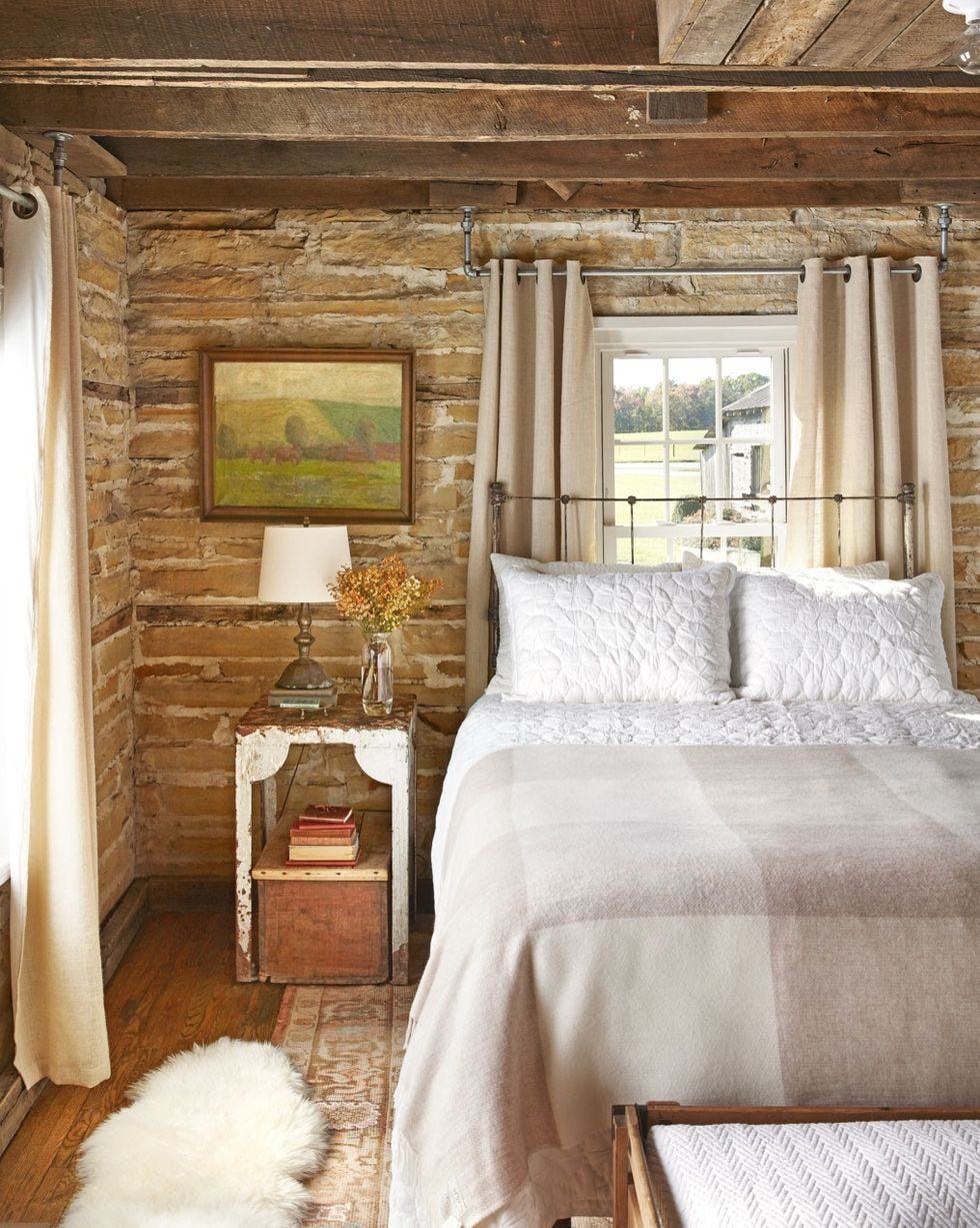 rustic bedroom with roughhewn stone walls and iron bed with neutral bedding