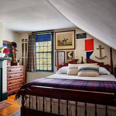 framed art and maps cover the walls of this nautical themed bedroom and the bed has a plaid spread and striped pillows