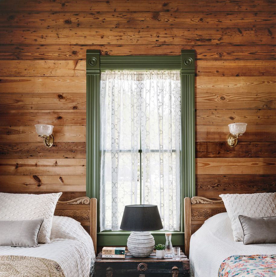 pine shiplap walls in a bedroom that has two twin sized beds and a window in the middle with lace curtains