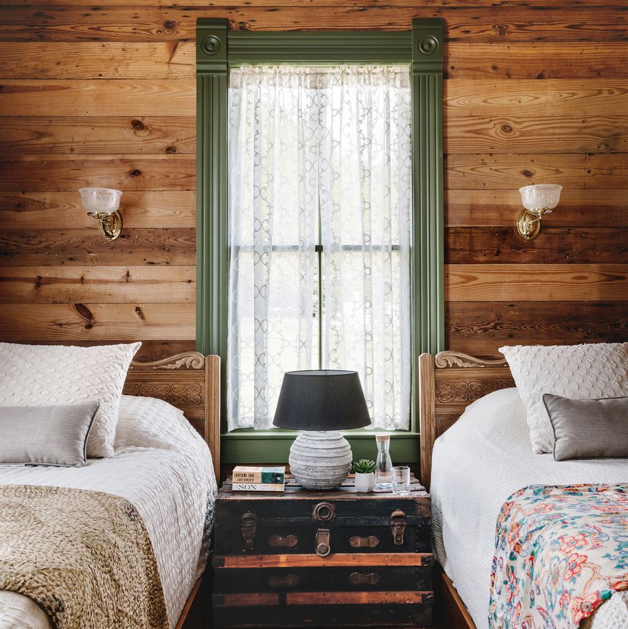 pine shiplap walls in a bedroom that has two twin sized beds and a window in the middle with lace curtains