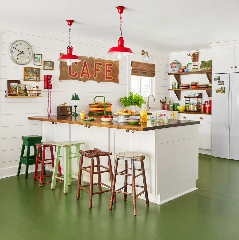 a cafe sign scored on a junking trip years ago is right at home in this missouri lake house kitchen where the colorful collected kitchen includes painted floors and a hodgepodge of counter stools and other nostalgic pieces