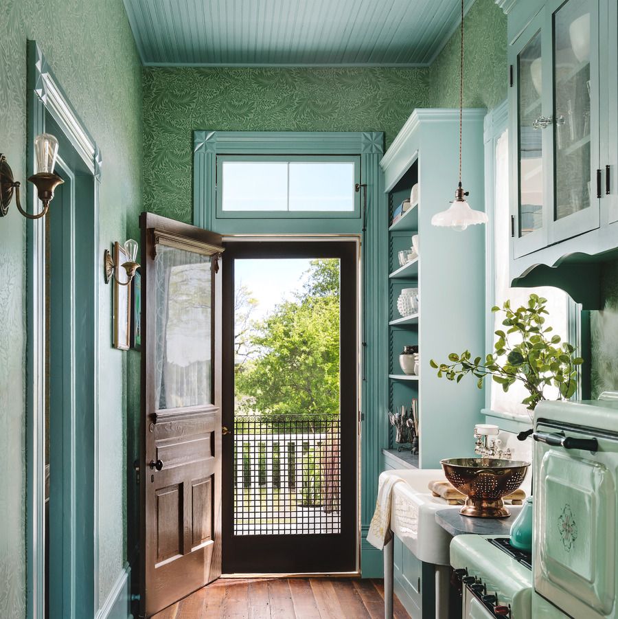 a tiny galley kitchen is painted in a pretty teal blue green color on the trim and cabinets and ceiling while a green wallpaper covers the walls