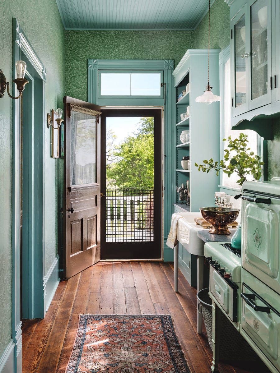 a tiny galley kitchen is painted in a pretty teal blue green color on the trim and cabinets and ceiling while a green wallpaper covers the walls