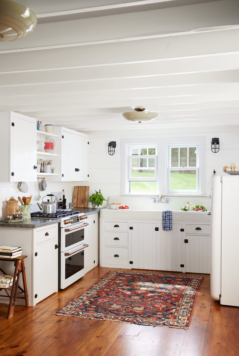 an all white corner kitchen with a colorful vintage rug over hardwood floors