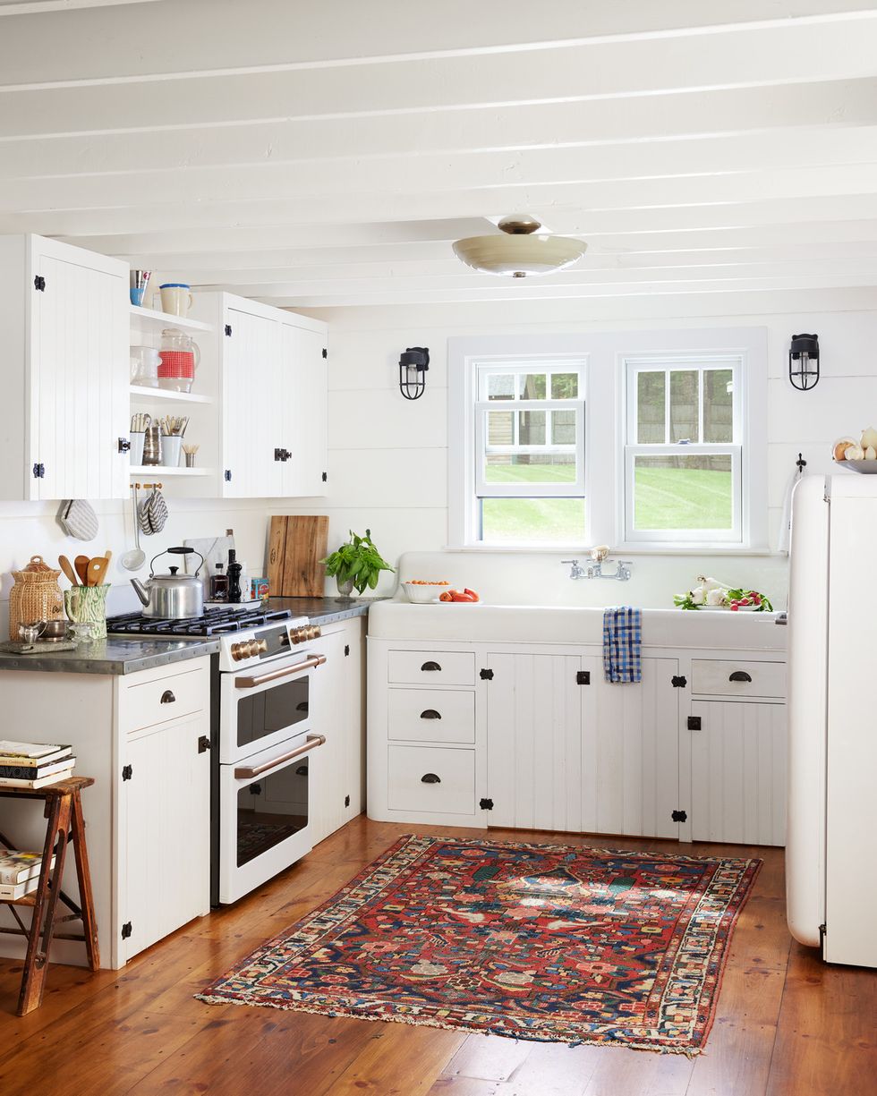 an all white corner kitchen with a colorful vintage rug over hardwood floors